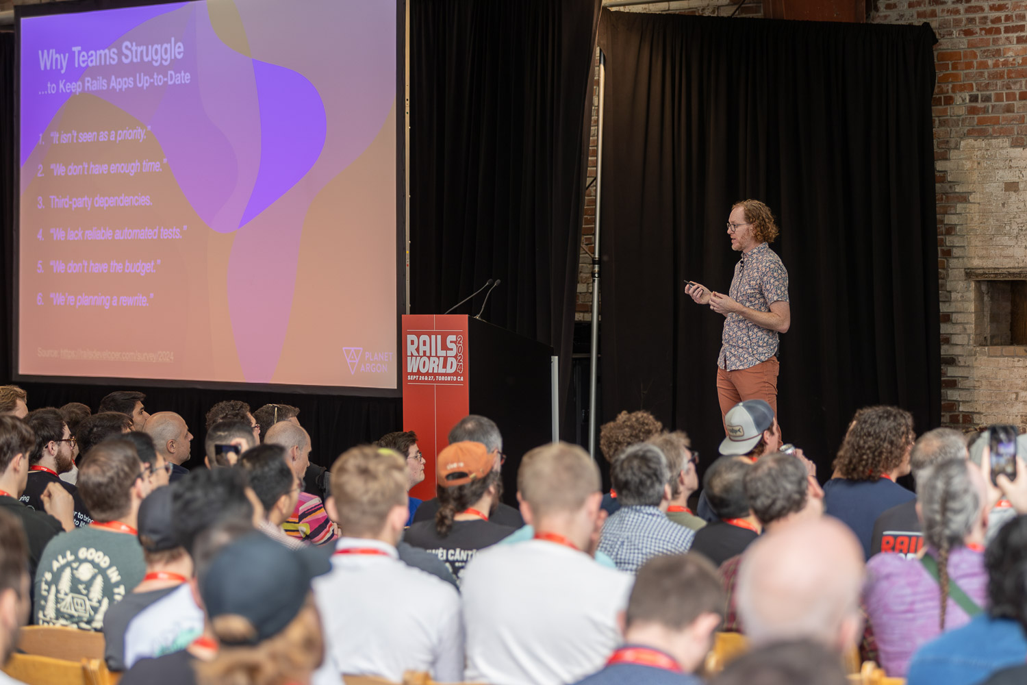 Robby Russell on stage at Rails World 2024, presenting a slide titled Why Teams Struggle to Keep Rails Apps Up-to-Date