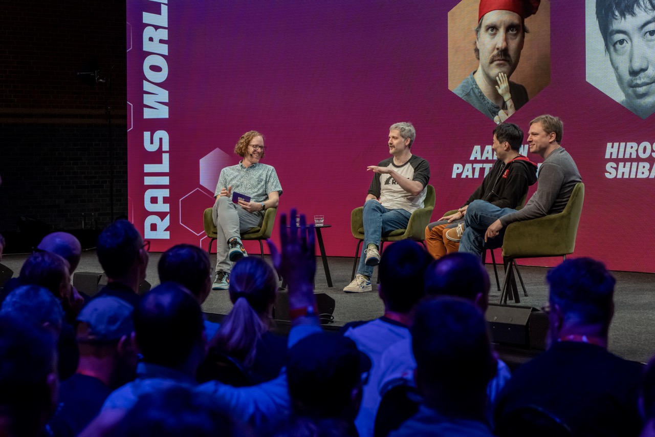 Robby Russell hosting a panel on stage at Rails World 2025 with Aaron Patterson, Hiroshi Shibata, and Jean Boussier